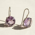 Silver-tone drop earrings with round faceted amethyst-purple stone in prong setting