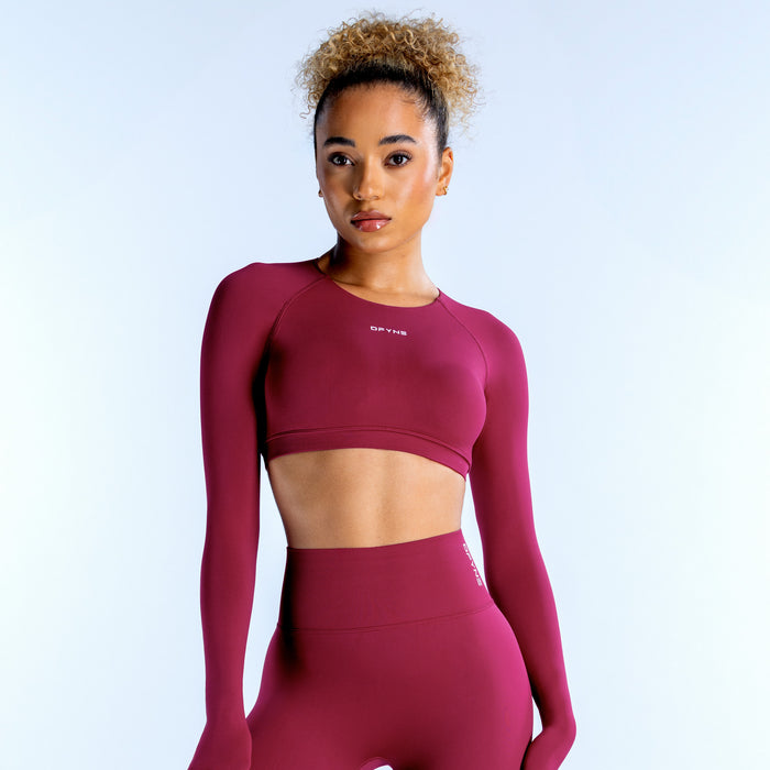 Magenta long-sleeve crop top with fitted crew neck and small logo on chest