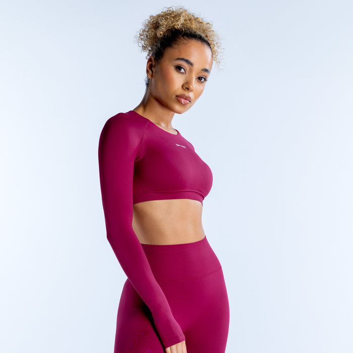 Magenta long-sleeve crop top with curved hem and subtle logo near shoulder