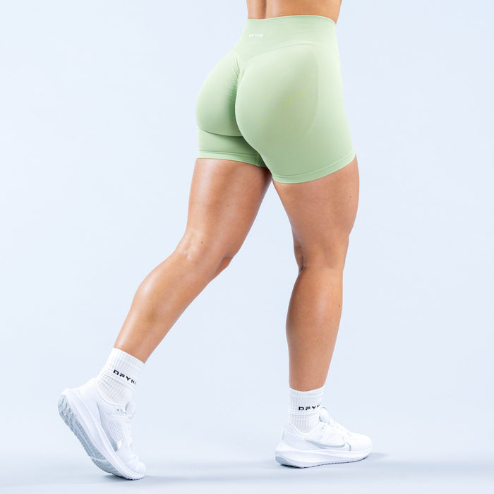 Mint green fitted athletic shorts with back seam, model standing in profile