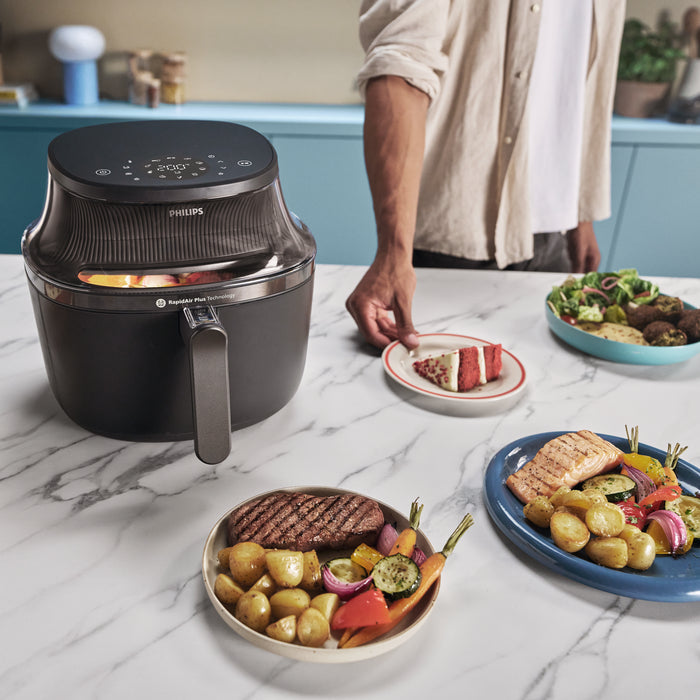 Philips air fryer on a kitchen counter with plates of food