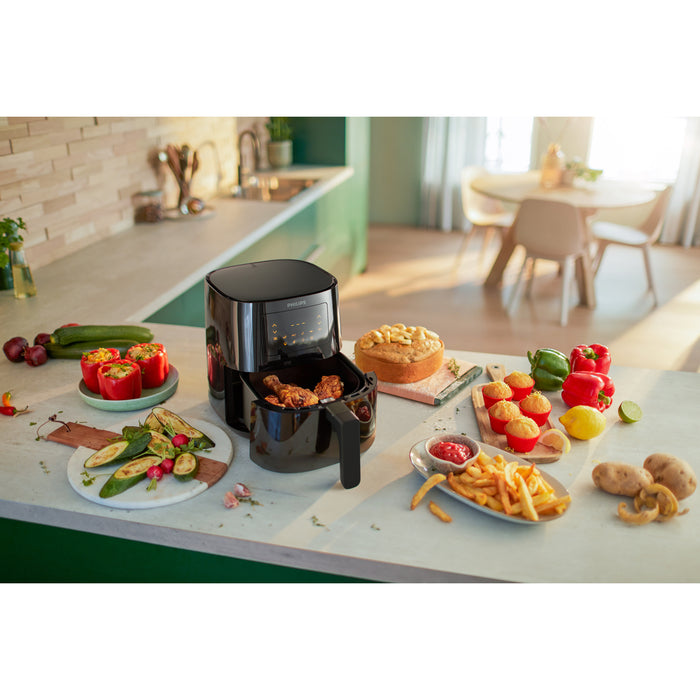 Black air fryer on a kitchen counter with various food items around