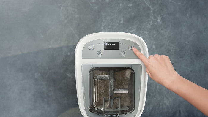 Hand pressing a button on a white electronic pasta maker with a screen on a gray background