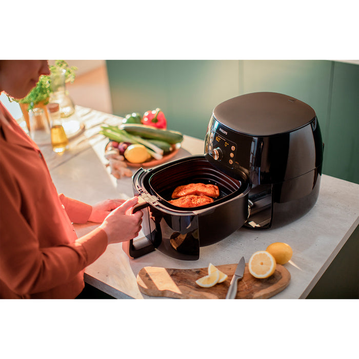 Person using a black air fryer with food on a kitchen counter.