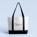 White and black tote bag with black handles and script logo front panel.