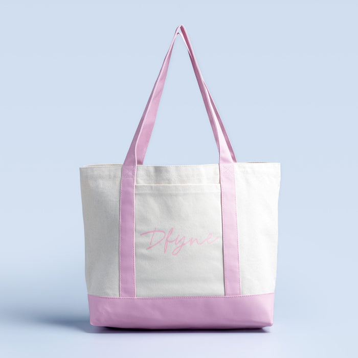 White canvas tote bag with lavender handles and bottom trim, cursive logo on front