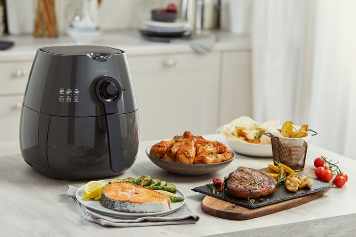Black air fryer on a kitchen counter with cooked food including salmon, chicken, and vegetables.
